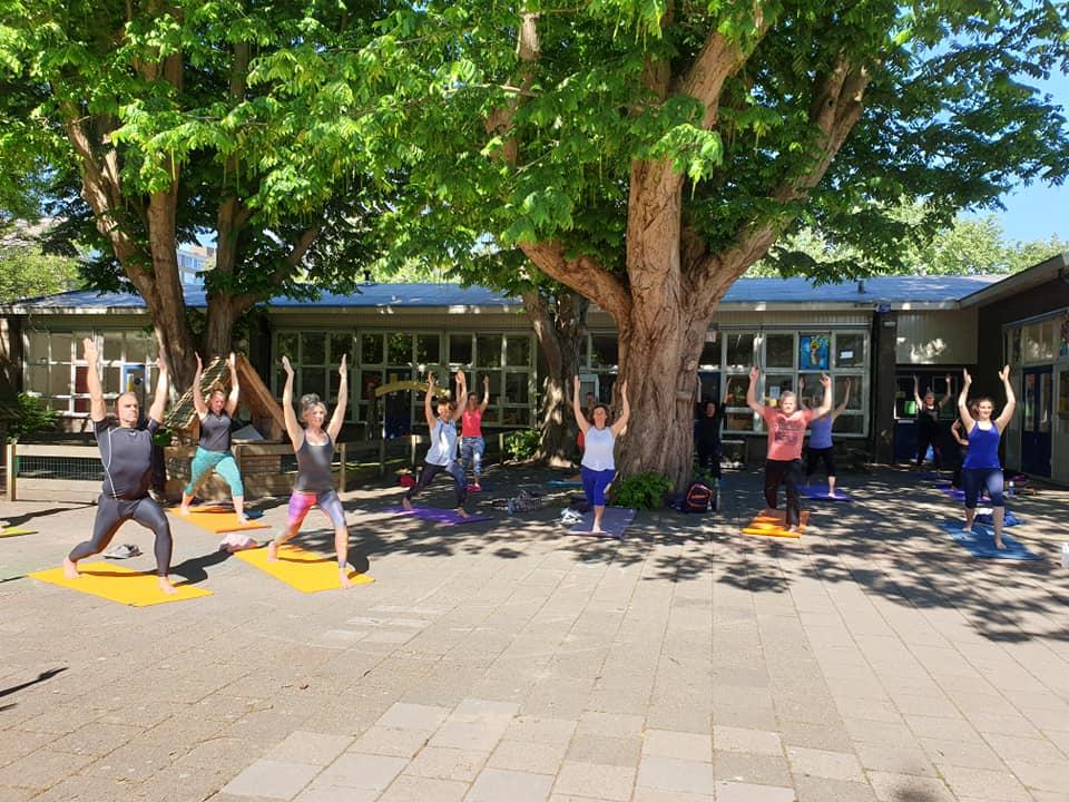 Een groep mensen doen yoga in de buitenlucht in de zon onder een grote boom bij Yoga en Co